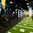 A modern gym space featuring a green track laid out on the floor with numbered lanes. TRX suspension trainers hang prominently in the foreground. The gym is equipped with various exercise equipment, including kettlebells and punching bags. In the background, there is a FIT sign near a reception desk under a low-ceilinged industrial design.